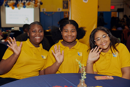 Happy students in NYC Great Oaks yellow uniform waving at camera
